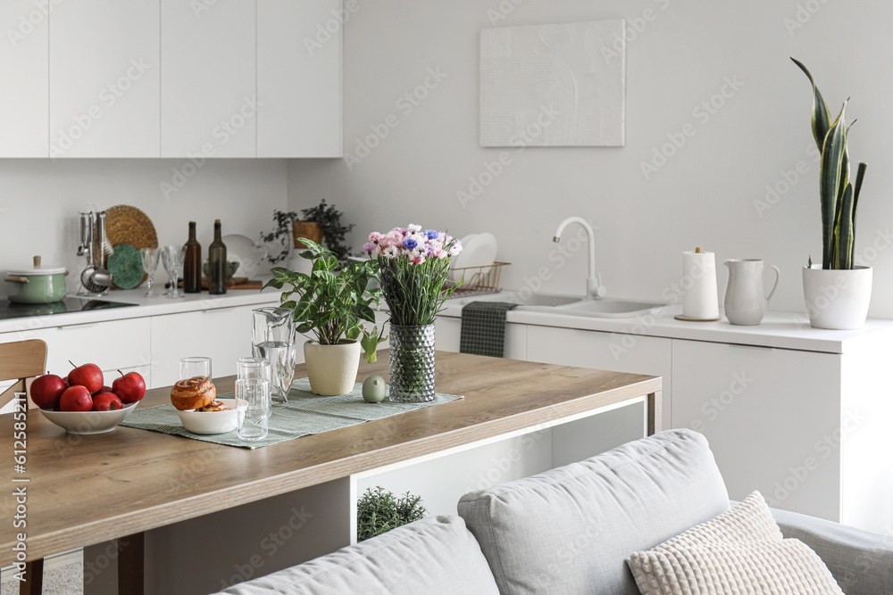 Island table with flowers and food in interior of light open space studio apartment