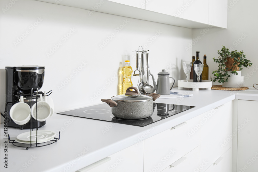 White countertop with electric stove, cooking pot and kitchenware