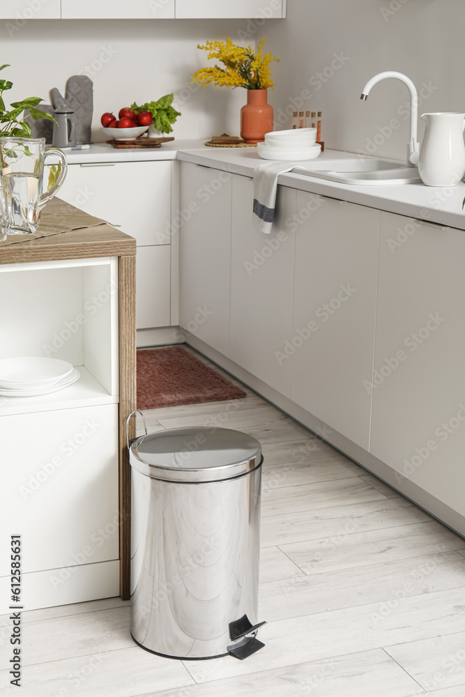 Metallic trash bin near table in interior of modern kitchen