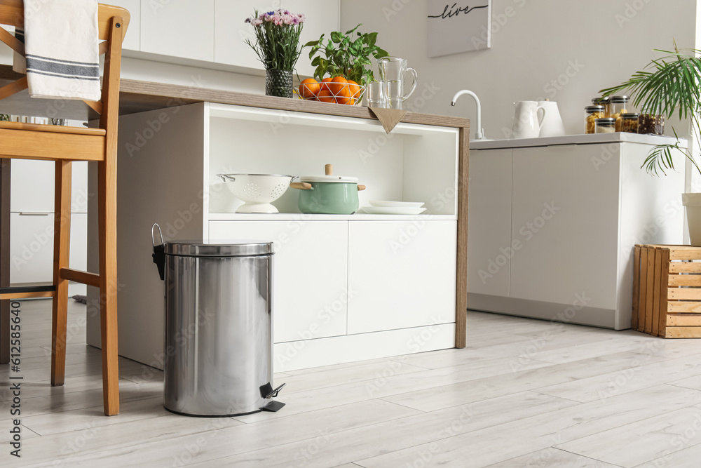 Metallic trash bin near table in interior of modern kitchen