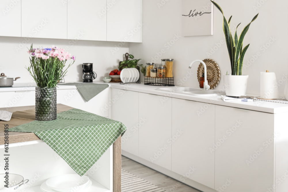 Interior of modern kitchen with flowers in vase on wooden island table