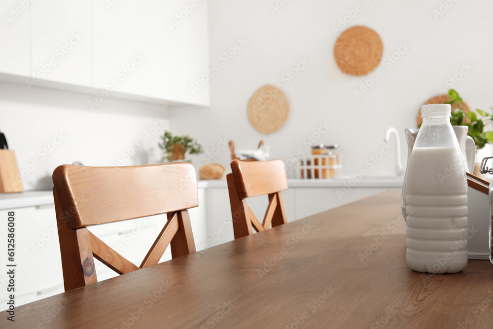 Wooden island table with bottle of milk and chairs in modern kitchen