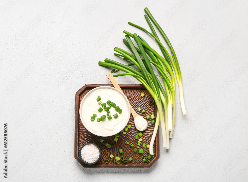 Tray with bowl of tasty sour cream and sliced green onion on white background