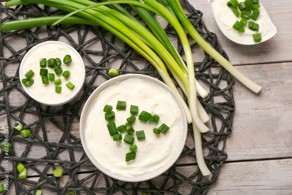 Bowls and gravy boat of tasty sour cream with sliced green onion on grey wooden background