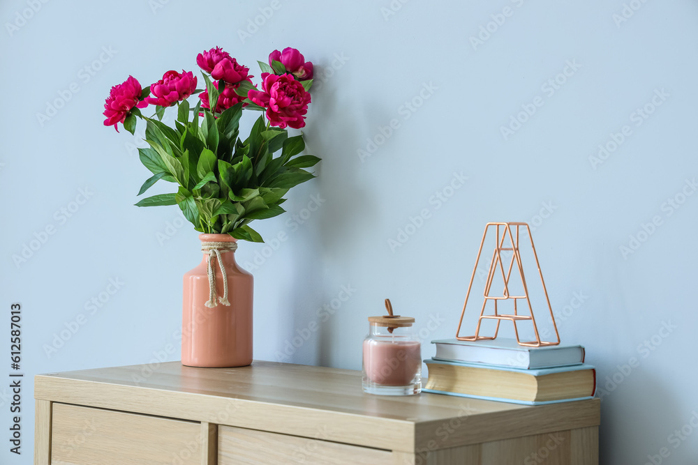 Vase with red peonies, candle and books on dresser near blue wall