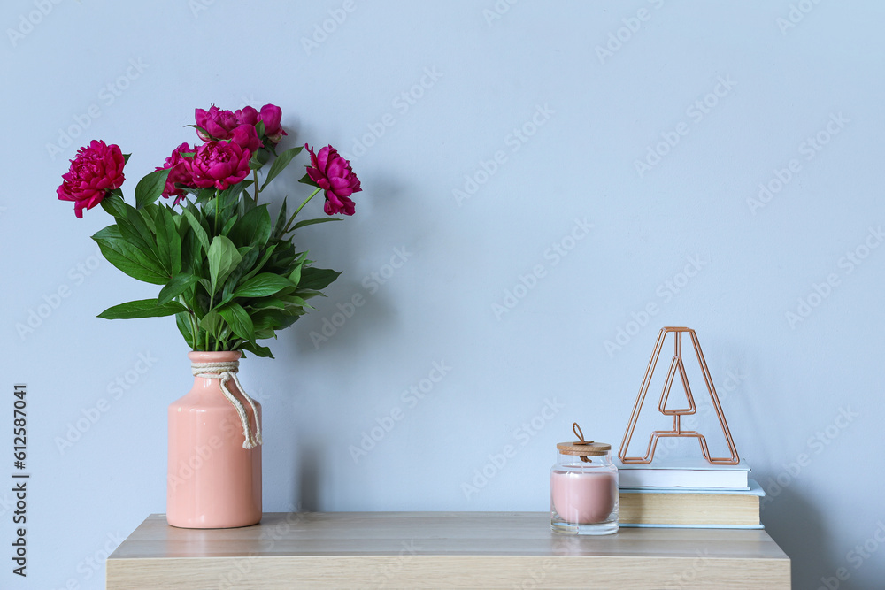 Vase with red peonies, candle and books on dresser near blue wall