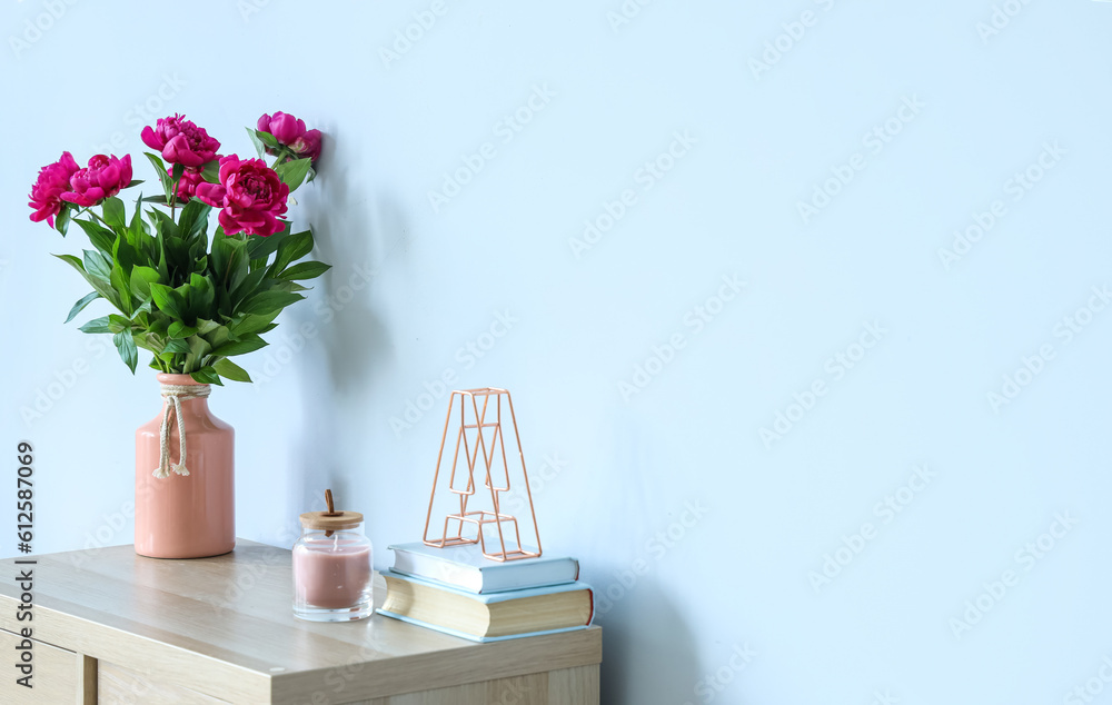 Vase with red peonies, candle and books on dresser near blue wall