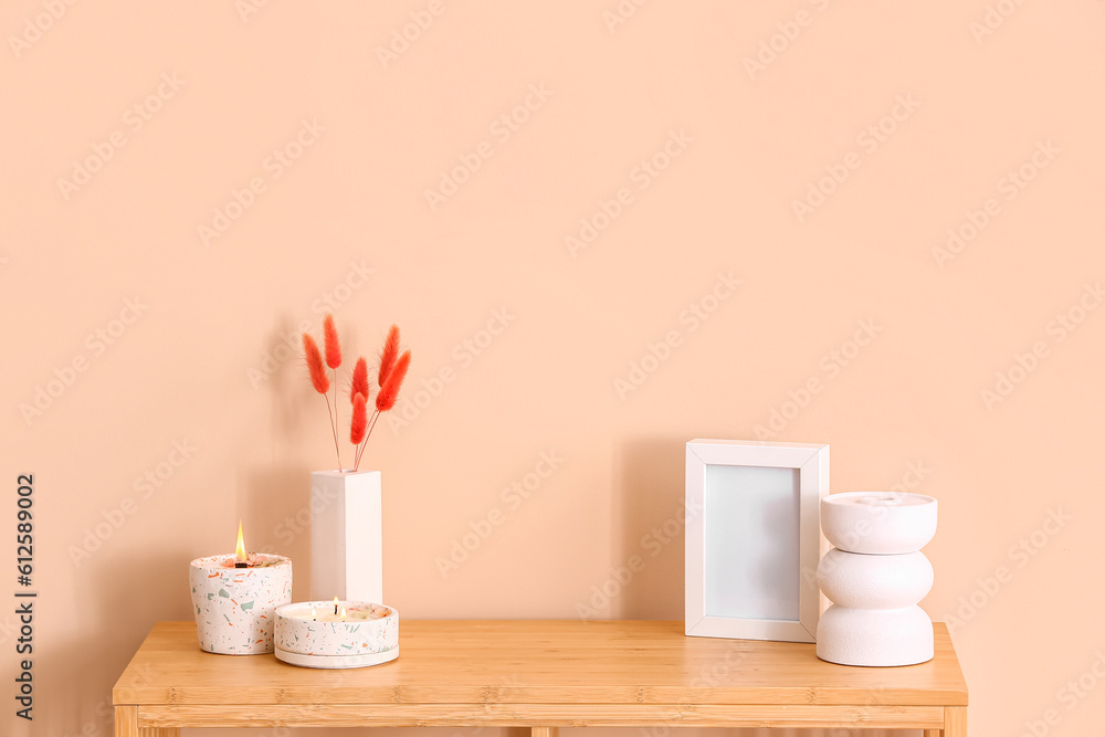 Holders with burning candles and blank frame on table near beige wall in room