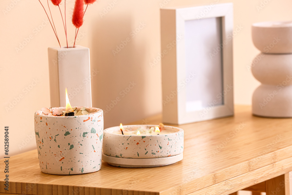 Holders with burning candles on table near beige wall in room, closeup