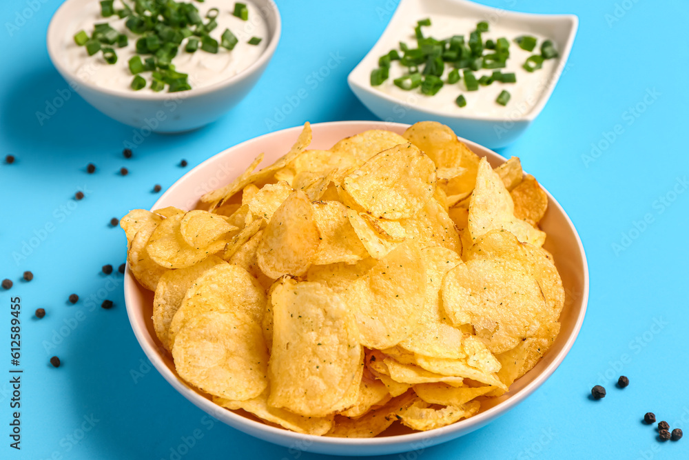 Bowls of tasty sour cream with sliced green onion and potato chips on blue background