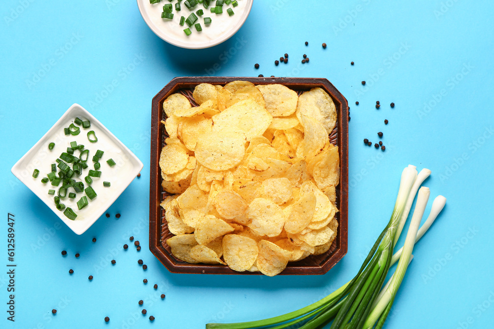 Bowls of tasty sour cream with sliced green onion and potato chips on blue background