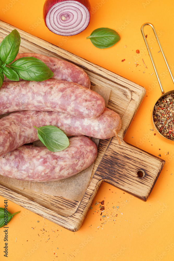 Board with raw fresh sausages and spices on orange background