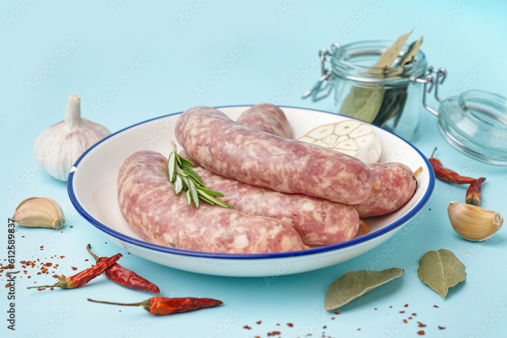 Plate with raw fresh sausages and spices on blue background, closeup