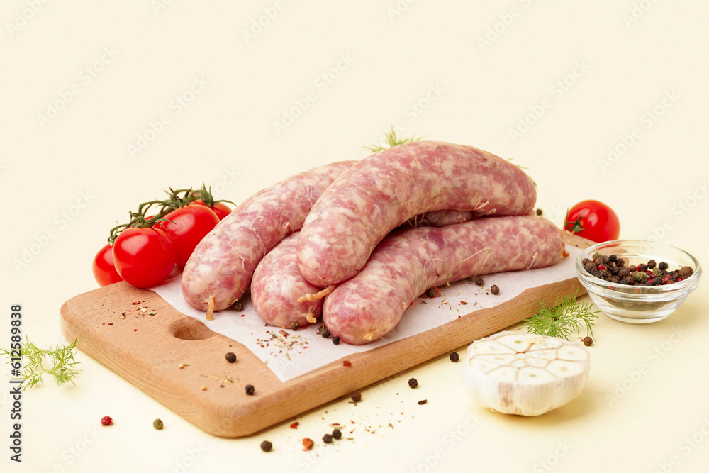 Board with raw fresh sausages, tomatoes and spices on beige background