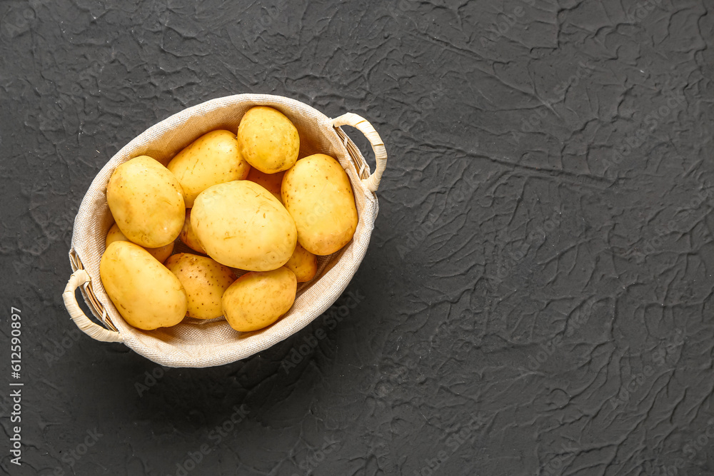 Wicker basket with raw baby potatoes on black background