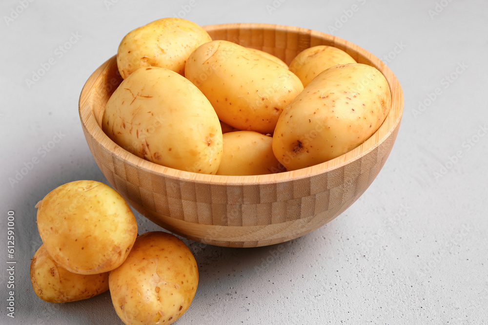 Wooden bowl with raw baby potatoes on grey background