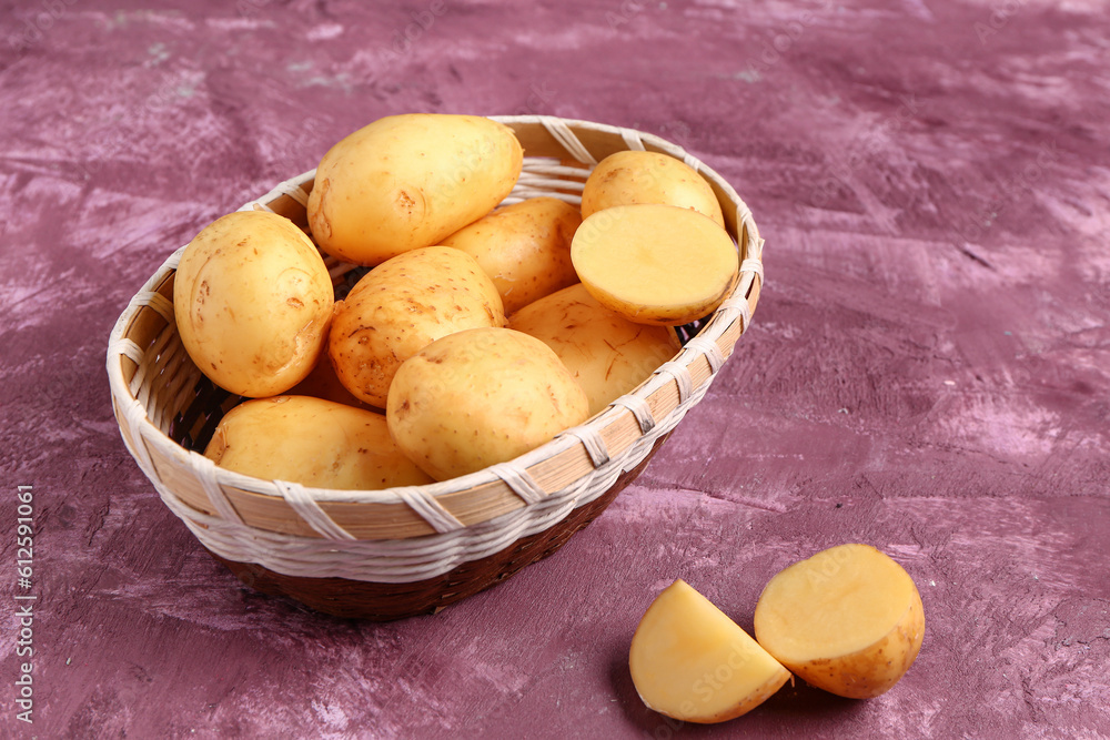 Wicker bowl with raw baby potatoes on purple background