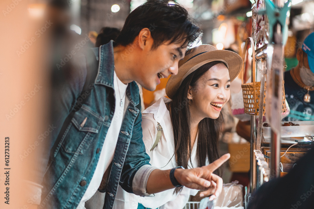 Asian couple tourist backpacker enjoying and eating street food in night market with crowd of people