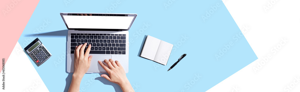 Person using a laptop computer with a notebook and a calculator