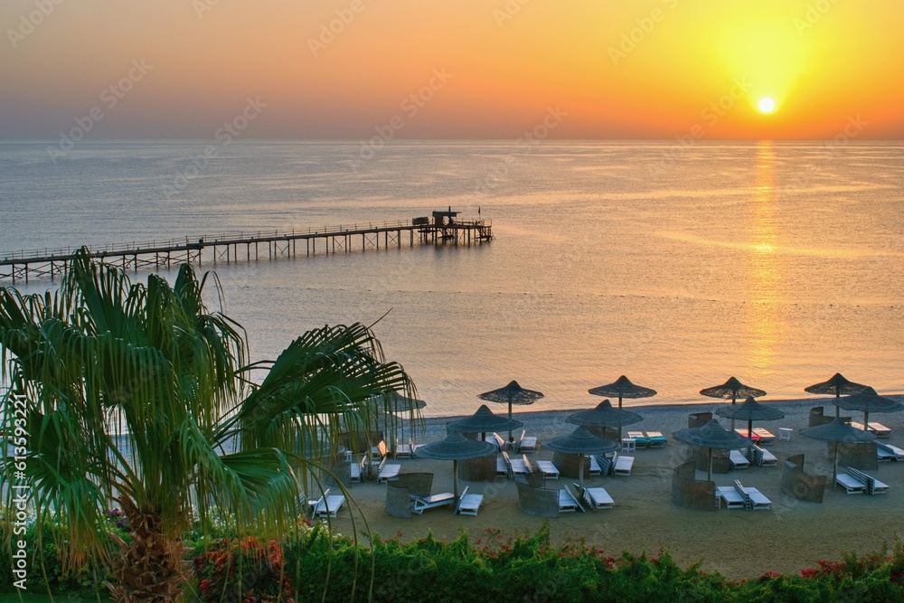 Sunrise on the idyllic beach with palms and sun umbrelas, Red Sea, Egypt