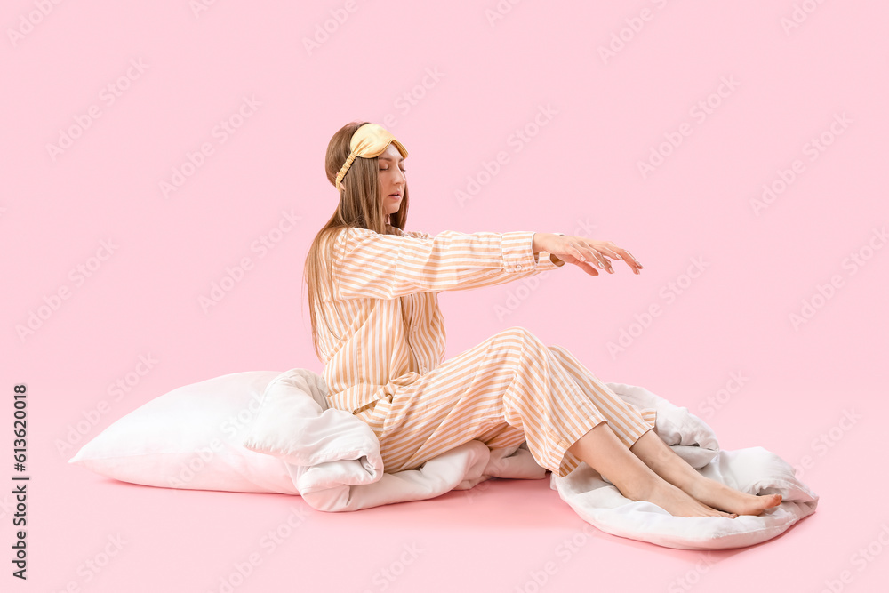 Young woman in pajamas with blanket and pillow on pink background