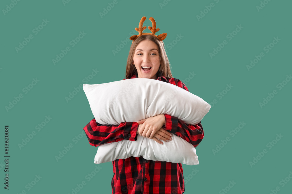 Young woman in reindeer horns with pillow on green background