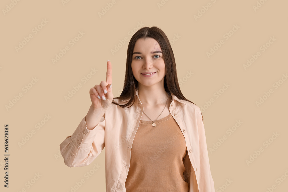 Young woman pointing at something on beige background