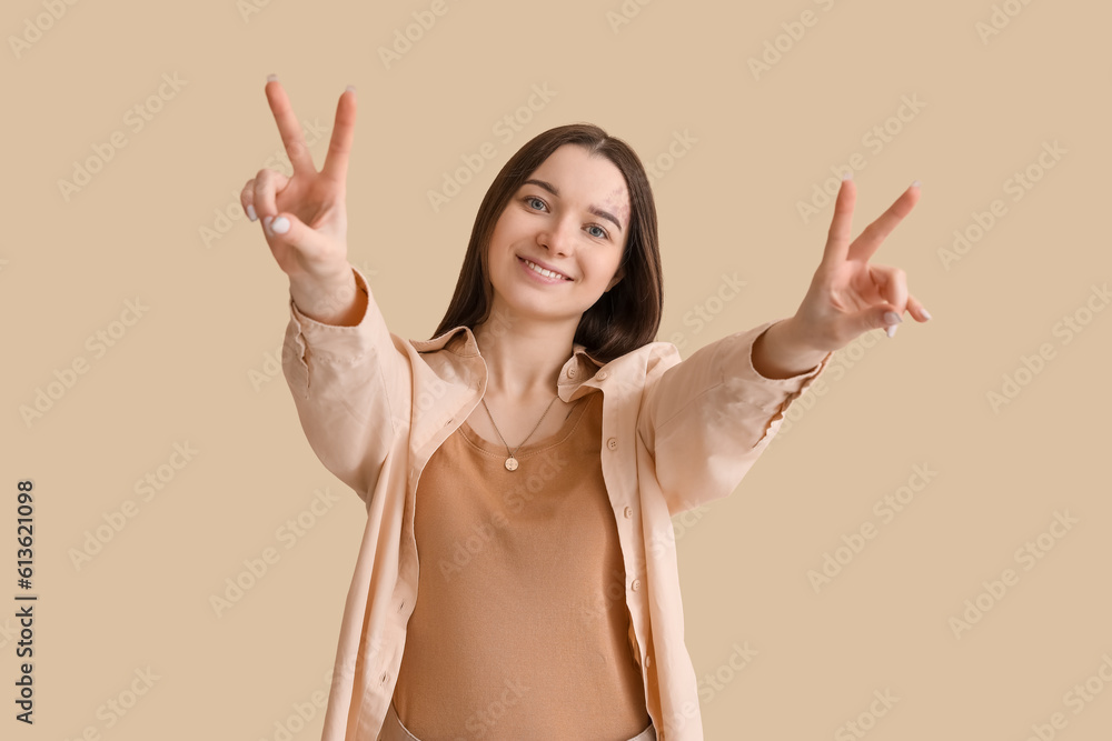 Young woman showing victory gesture on beige background