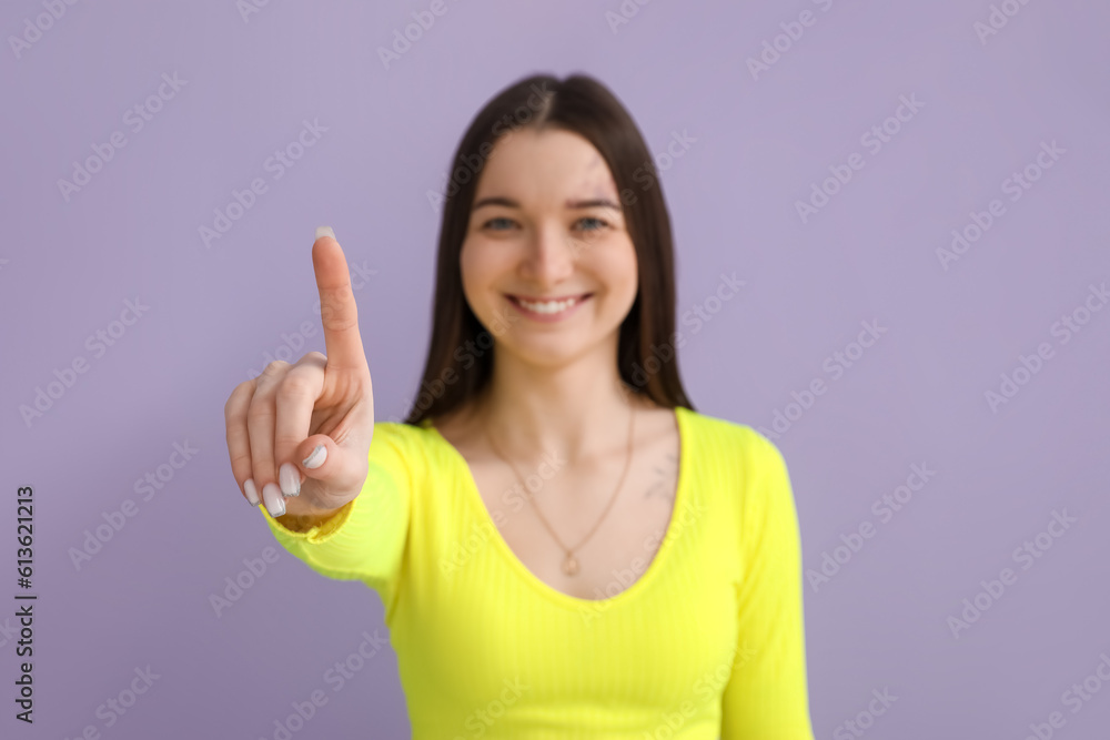 Young woman in bright shirt with raised index finger on lilac background, closeup