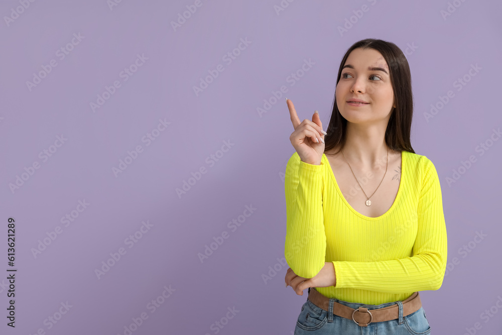 Young woman in bright shirt pointing at something on lilac background