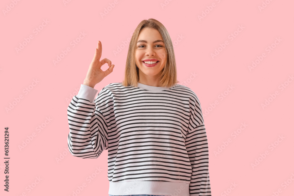 Young woman in striped sweatshirt showing OK on pink background