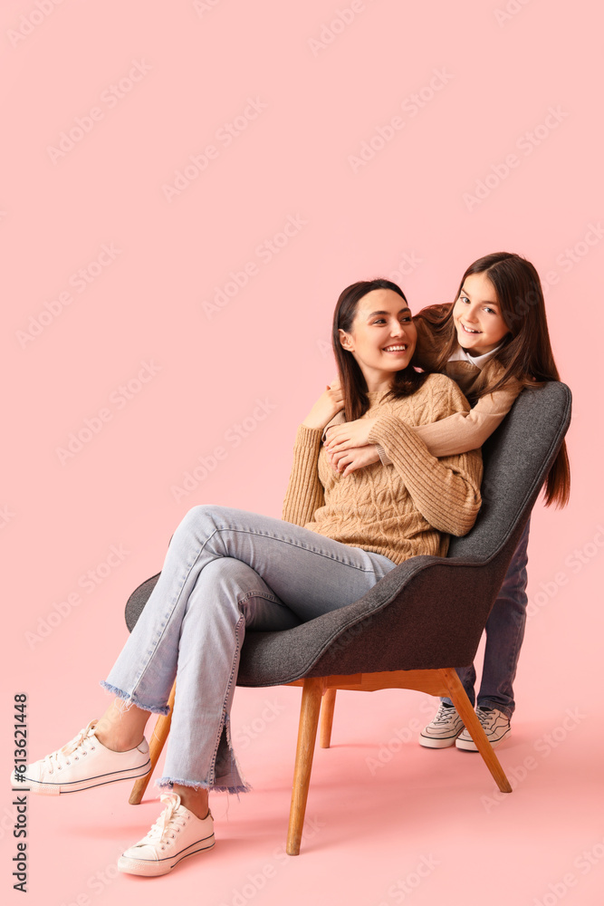 Little girl and her mother in knitted sweaters hugging on pink background