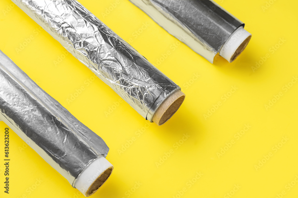 Aluminium foil rolls on yellow background, closeup