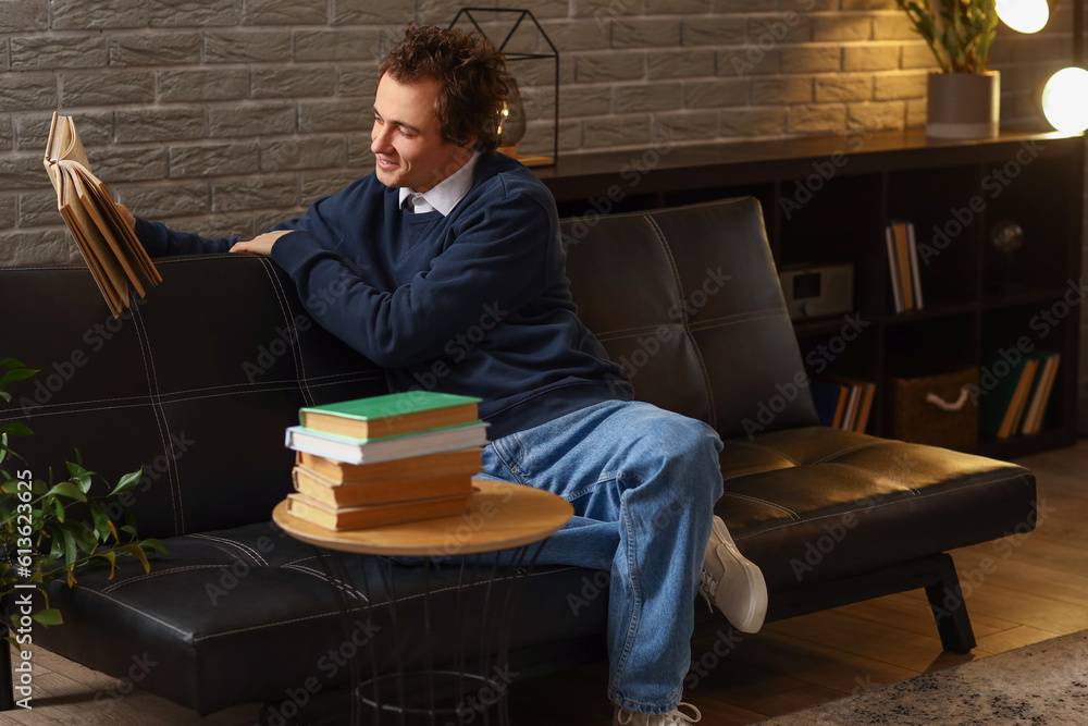 Young man reading book on sofa at home late in evening