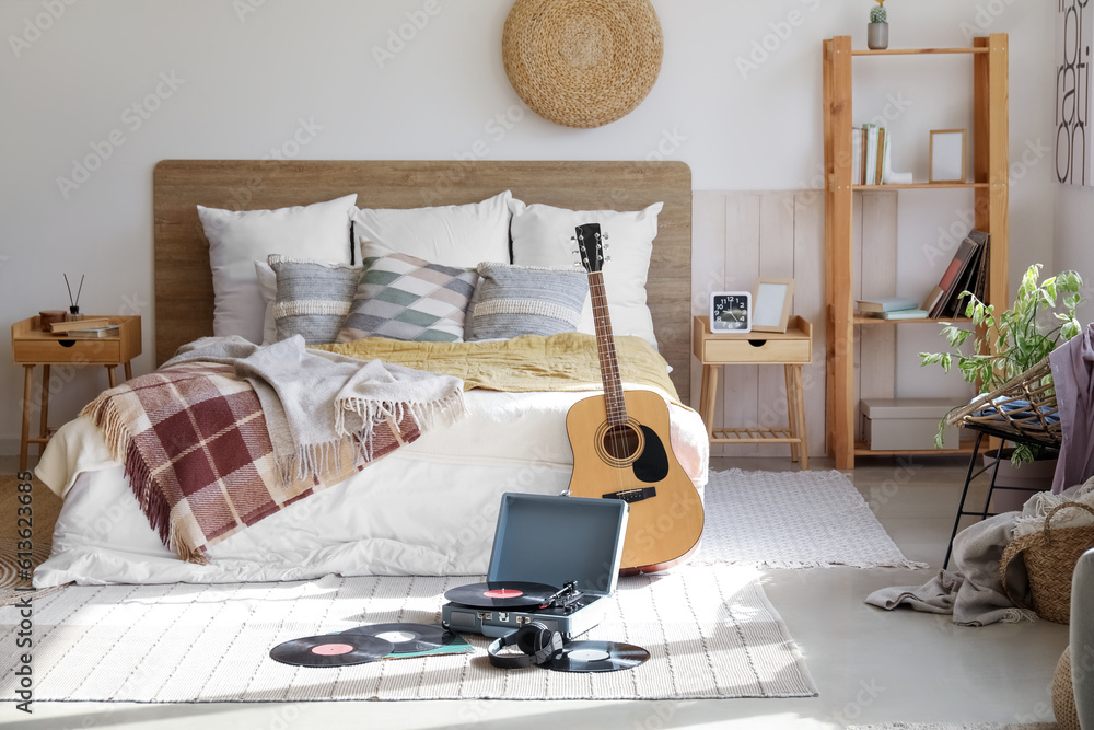 Record player with vinyl disks and guitar in interior of bedroom