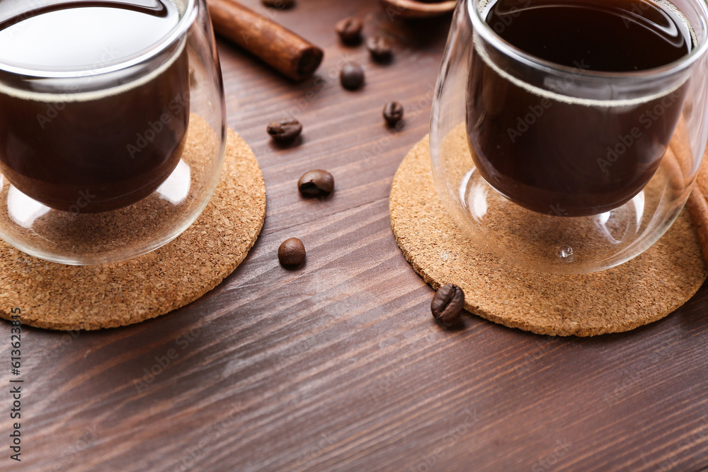 Drink coasters with glasses of coffee, cinnamon and beans on wooden table