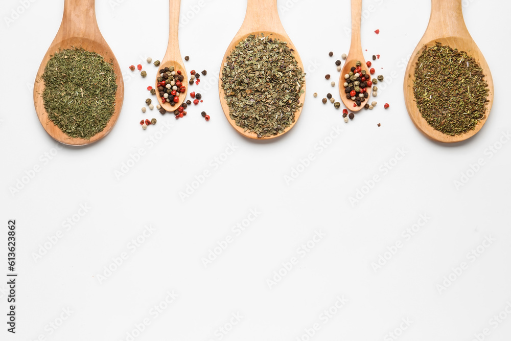 Wooden spoons with dried herbs and peppercorns on light background