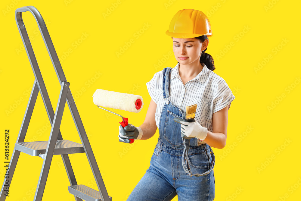 Female decorator with paint roller and brush on yellow background