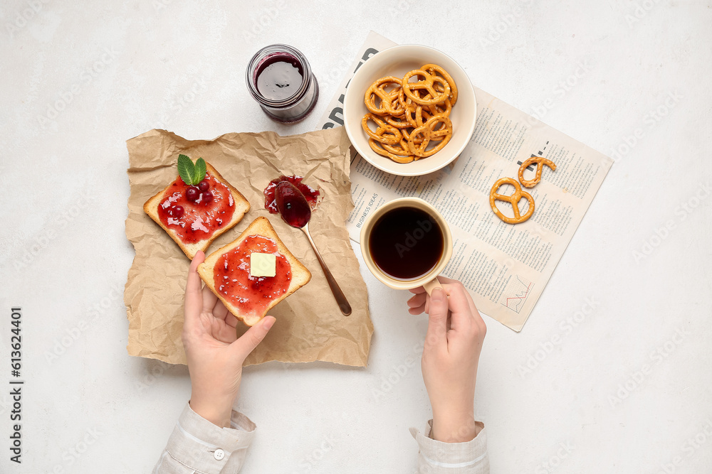 Woman eating tasty toasts with cranberry jam and drinking coffee on light background