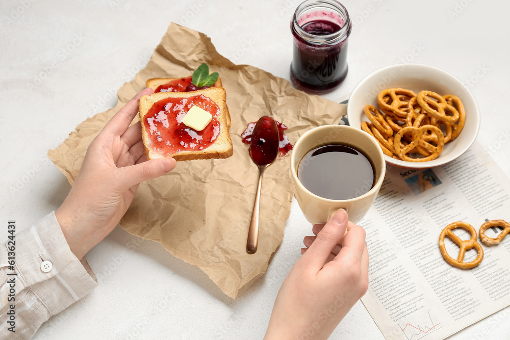 Woman eating tasty toasts with cranberry jam and drinking coffee on light background