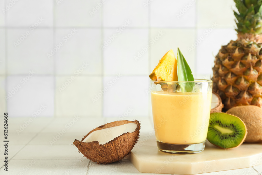 Glass of tasty pineapple smoothie, kiwi and coconut on tile table