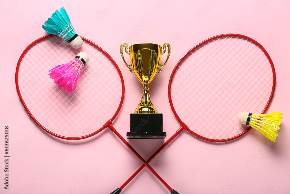 Gold cup with badminton rackets and shuttlecocks on pink background