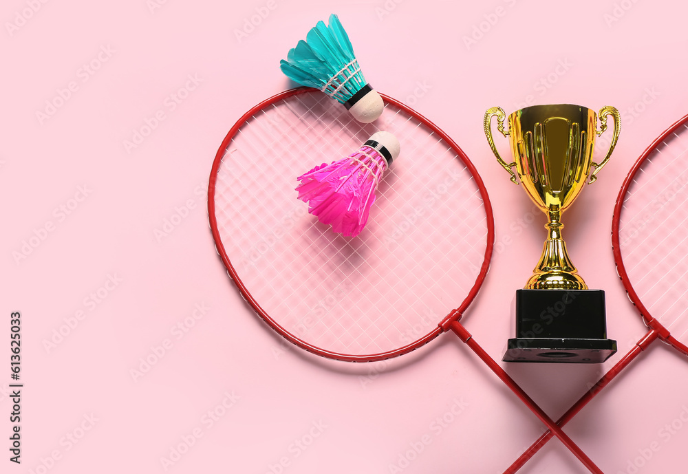 Gold cup with badminton rackets and shuttlecocks on pink background