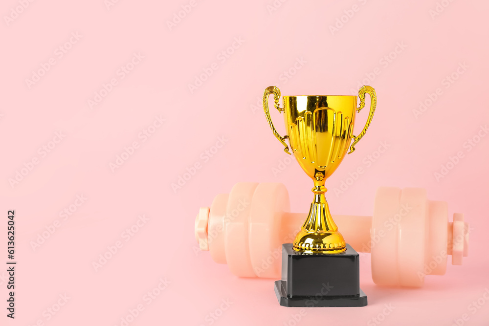 Gold cup with dumbbell on pink background