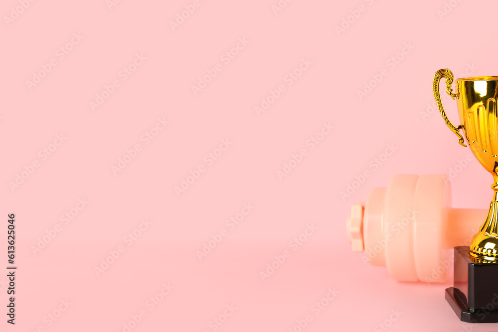 Gold cup with dumbbell on pink background