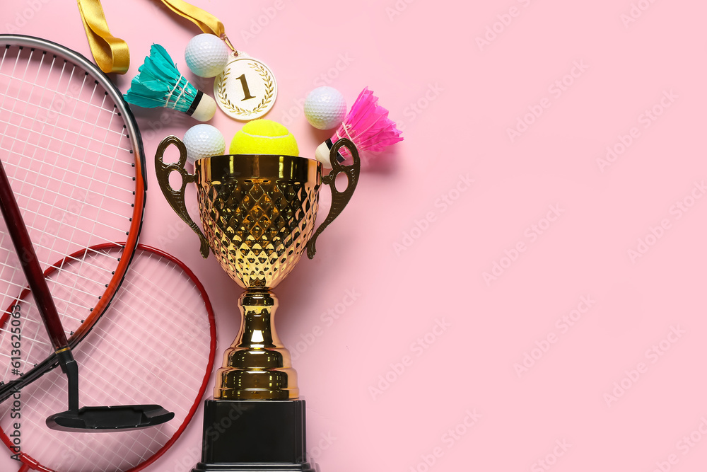 Gold cup with first place medal and sports equipment on pink background