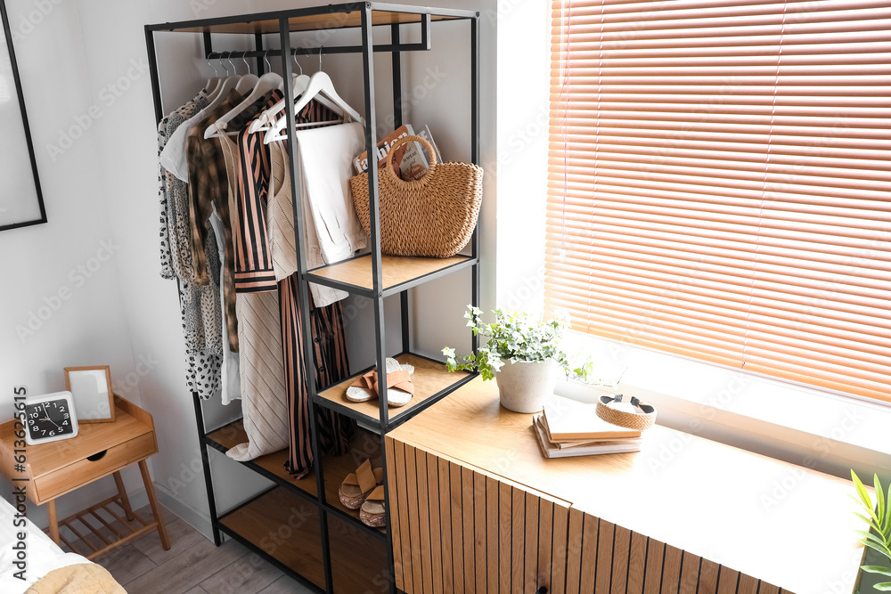 Interior of light bedroom with shelving unit and clothes