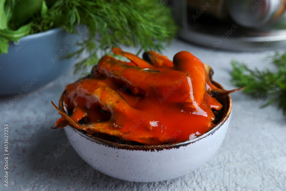 Bowl with canned fish in tomato sauce on grey table