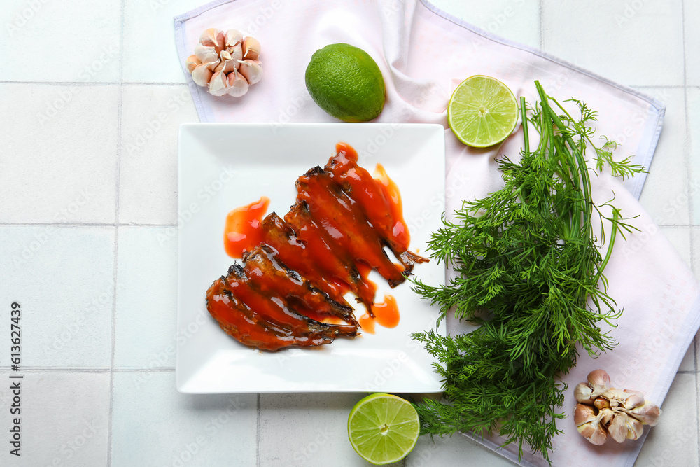 Plate with canned fish in tomato sauce, lime, garlic and dill on white tiled table