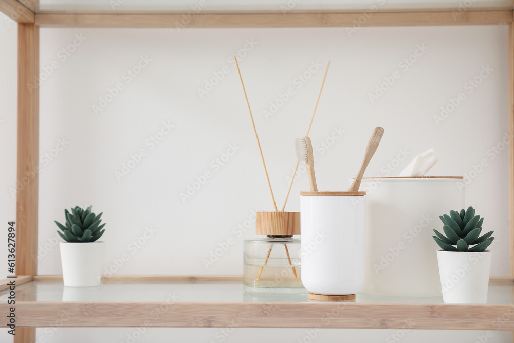 Bath accessories with reed diffuser and houseplants on shelf near light wall